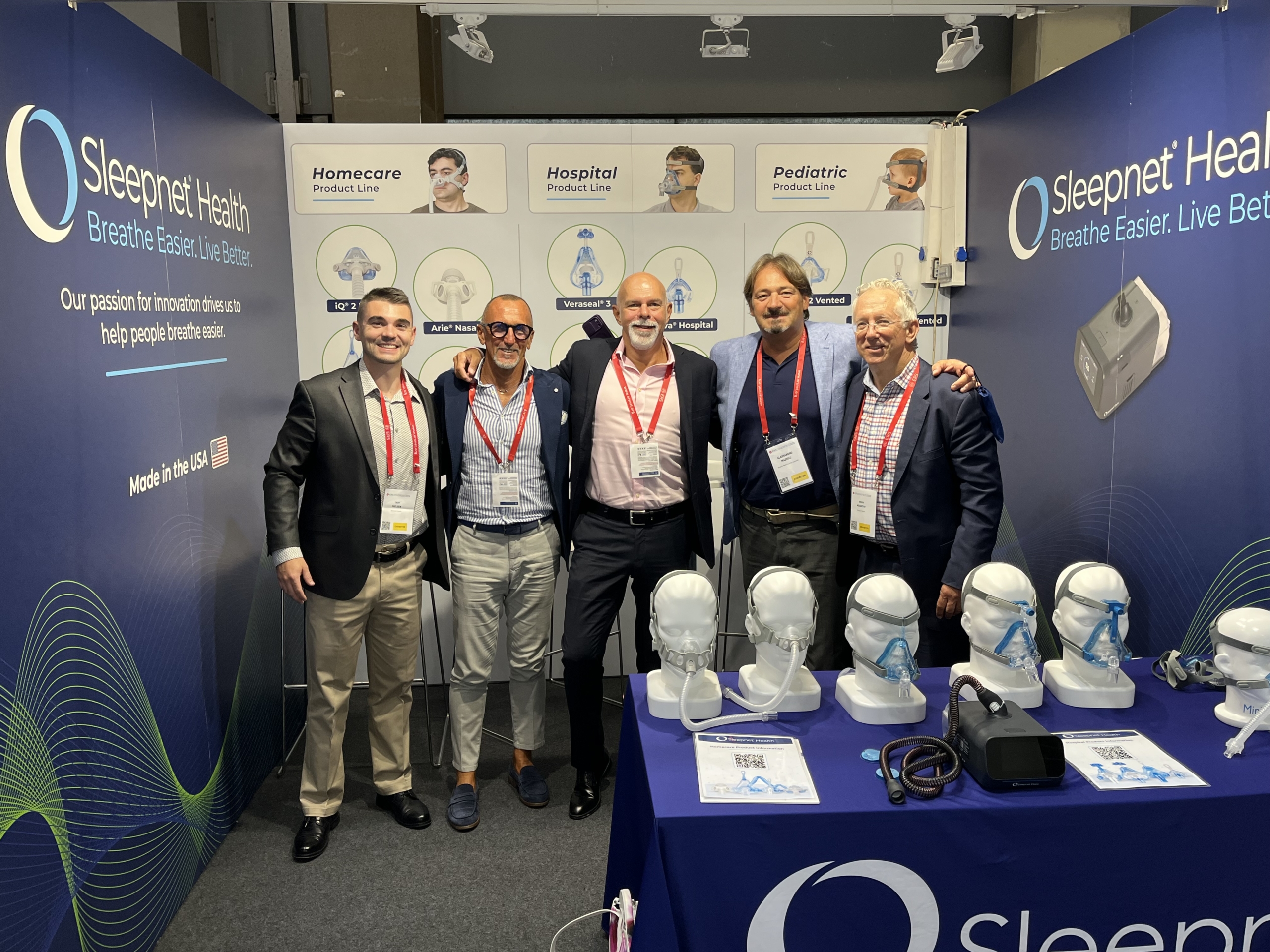 IMG_0855 - Sleepnet Corporation Five men in business attire pose together at a Sleepnet Health booth with CPAP masks on display in the foreground.